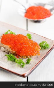 Sandwich with red caviar at plate on white table, closeup