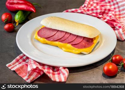Sandwich with salami and cheddar on dark stone table