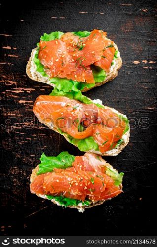 Sandwich with salmon and herbs. Against a dark background. High quality photo. Sandwich with salmon and herbs.
