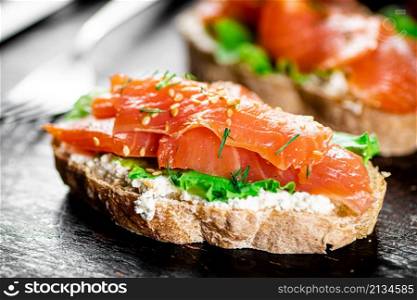 Sandwich with salmon and herbs. Against a dark background. High quality photo. Sandwich with salmon and herbs.