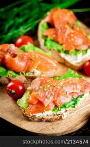 Sandwich with salmon and herbs on a cutting board. Macro background. High quality photo. Sandwich with salmon and herbs on a cutting board.
