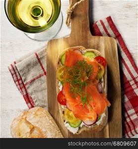 Sandwich with salmon, cucumber, cream cheese, dill and tomatoe on rustic wooden background.