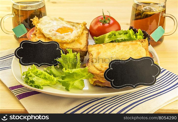 Sandwiches and tea cups for a pair - Plate with sandwiches, fried egg, tomato and green salad on wooden table. Each sandwich has a blank paper tag for short messages.