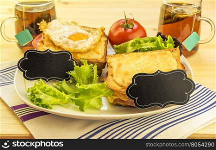 Sandwiches and tea cups for a pair - Plate with sandwiches, fried egg, tomato and green salad on wooden table. Each sandwich has a blank paper tag for short messages.