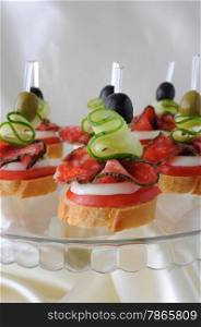 Sandwiches (canapes) of salami with olives on a plate