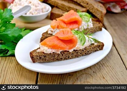 Sandwiches on two pieces of rye bread with cream, dill, cucumber and salmon in a white plate on a wooden boards background