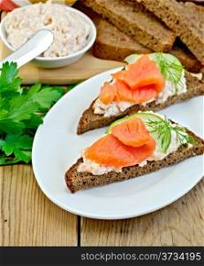 Sandwiches on two pieces of rye bread with cream, dill, cucumber and salmon in the oval plate on the background of wooden boards