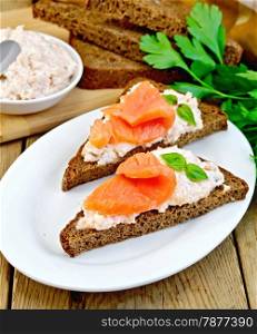 Sandwiches on two triangular pieces of rye bread with cream, basil and salmon, knife, napkin, parsley on a wooden boards background