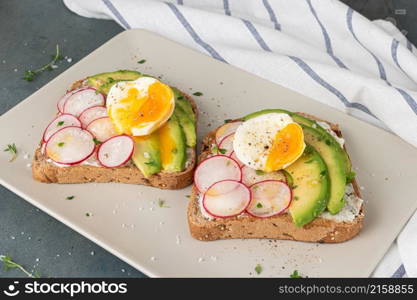 Sandwiches with avocado radish cheese and eggs on a rye bread on plate on dark background. Healthy breakfast. Vegetarian food.