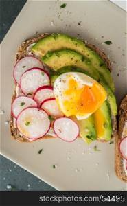 Sandwiches with avocado radish cheese and eggs on a rye bread on wooden board on dark background. Healthy breakfast. Vegetarian food