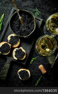 Sandwiches with black caviar, caviar in a bowl and white wine. On black rustic background. Sandwiches with black caviar, caviar in a bowl and white wine.
