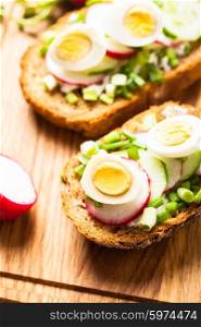Sandwiches with fresh radish, cucumber, onions and quail eggs on a wooden table