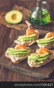 Sandwiches with guacamole, sliced avocado and shrimps on the wooden board