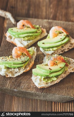 Sandwiches with guacamole, sliced avocado and shrimps on the wooden board