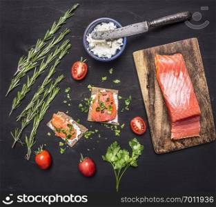 sandwiches with pink salmon fillet, curd cheese, herbs and cherry tomatoes on wooden rustic background top view close up