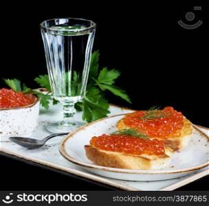 Sandwiches with red caviar and glass of vodka on a porcelain plate isolated at black