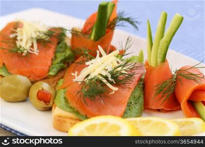 Sandwiches with salmon, cheese, lettuce, herbs on plate, olives and lemons.