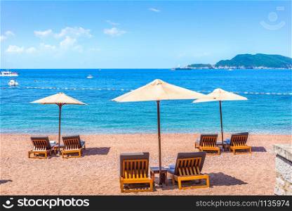 Sandy beach in Sveti Stefan with chaise-longues and umbrellas at summer day, Montenegro. Beach in Sveti Stefan