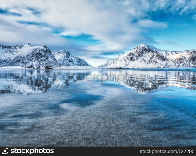 Sandy beach with beautiful reflection in water, Lofoten islands, Norway. Landscape with snowy mountains, sea, blue sky with clouds reflected in water in winter. Nature background with rocks and coast. Sandy beach with beautiful reflection in water, Lofoten islands,