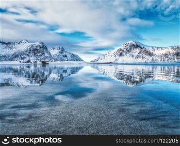 Sandy beach with beautiful reflection in water, Lofoten islands, Norway. Landscape with snowy mountains, sea, blue sky with clouds reflected in water in winter. Nature background with rocks and coast. Sandy beach with beautiful reflection in water, Lofoten islands,