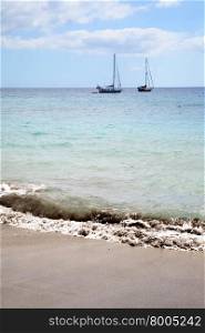 Sandy beach with surf and two sailing yachts