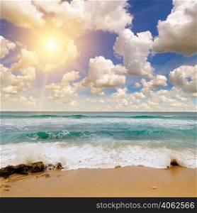 Sandy tropical beach, blue ocean water and bright sunrise.