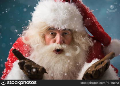 Santa Claus blowing snow and looking at camera outdoors in winter