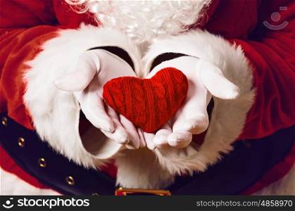 Santa Claus holding gift. Santa Claus holding red knitted heart in both hands