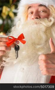 Santa Claus holding keys of new house or apartment and thumbs up, standing near Christmas tree. Good mortgage offer concept