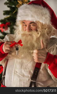 Santa Claus holding keys of new house or apartment and thumbs up, standing near Christmas tree. Good mortgage offer concept