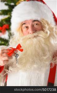 Santa Claus holding keys with red ribbon standing near Christmas Tree. New year - new home concept