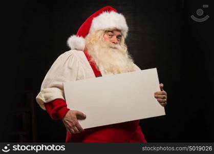 Santa Claus holding white blank sign with fun and smile standing against dark background