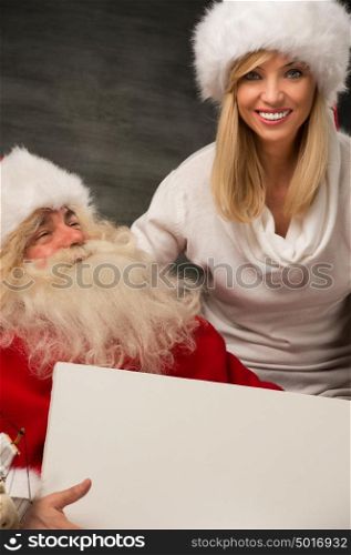 Santa Claus holding white blank sign with his wife and helper