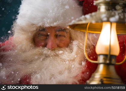 Santa Claus is holding a shining lantern while sneaking to his home outdoors at North Pole