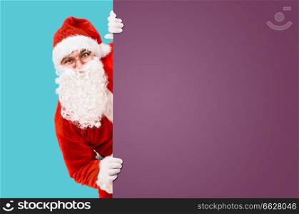 Santa Claus is looking out of colorful advertisement board and copy space. Santa Claus with colorful advertisement board