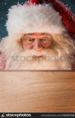 Santa Claus looking into wooden box outdoors. Light is coming from inside to his face. Opening Christmas magic concept.