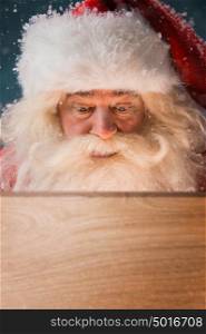 Santa Claus looking into wooden box outdoors. Light is coming from inside to his face. Opening Christmas magic concept.