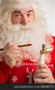 Santa Claus making toys. Painting and coloring christmas decoration of angel statuette