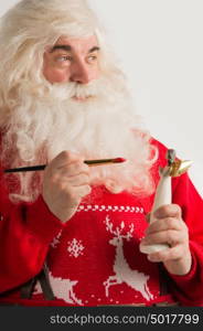 Santa Claus making toys. Painting and coloring christmas decoration of angel statuette