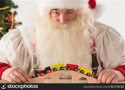 Santa Claus sitting and playing with railway toy at home