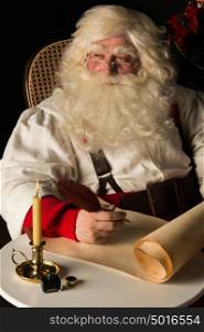 Santa Claus sitting at home and writing on old paper roll to do list with quill pen and ink at night with candle light. Authentic vintage style portrait.