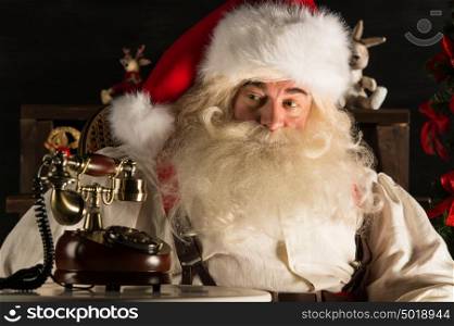 Santa Claus sitting at home near Christmas tree and waiting a call. Vintage phone standing at table near him