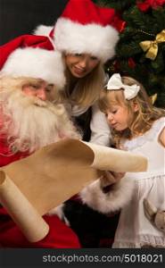 Santa Claus sitting at home with cute little girl and her mother and reading letter