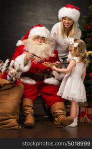 Santa Claus sitting at home with family - little girl and her mother and painting Christmas decorations
