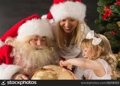 Santa Claus sitting at home with family - little girl and her mother and looking at globe all together