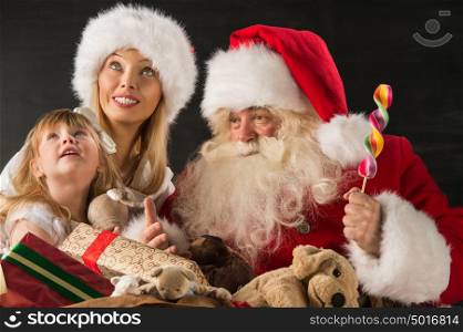 Santa Claus sitting at home with family - little girl and her mother and giving gifts