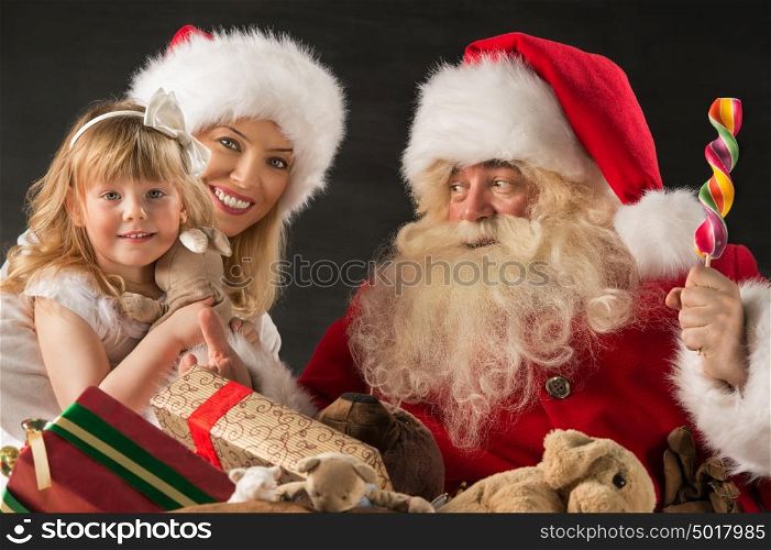 Santa Claus sitting at home with family - little girl and her mother and giving gifts