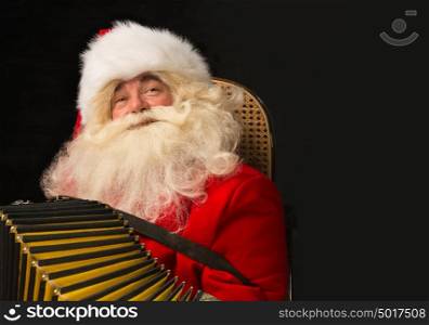 Santa Claus sitting in armchair at home and playing music on accordion. Christmas party merriment. Lots of copyspace