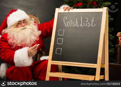 Santa Claus sitting near chalkboard with wishlist sign and blank copy space for checkboxes and your text