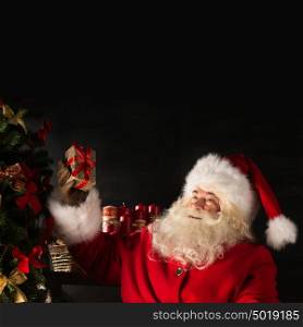 Santa Claus standing near Christmas tree in dark room. Lots of copyspace